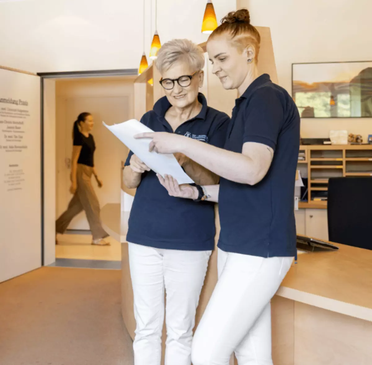 Zwei Mitarbeiterinnen stehen am Empfang und schauen sich gemeinsam Unterlagen an