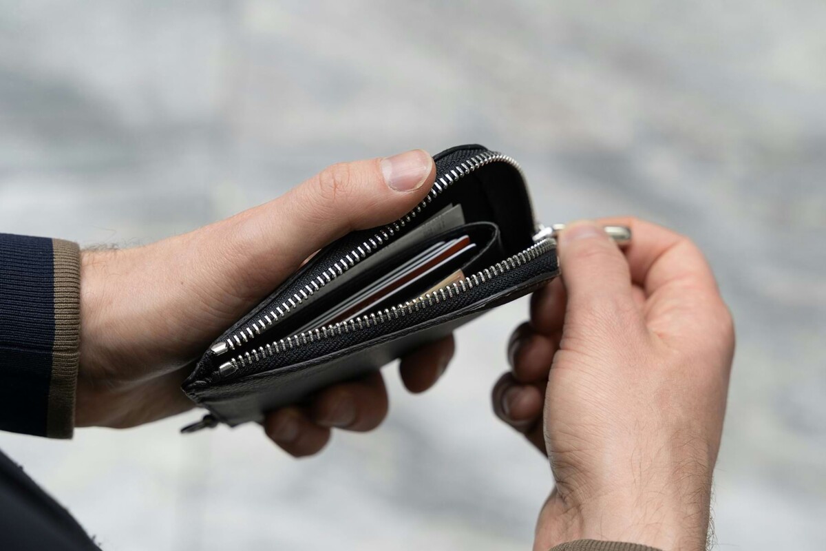 Detailaufnahme einer Person, die den Reißverschluss eines Geldbeutels öffnet