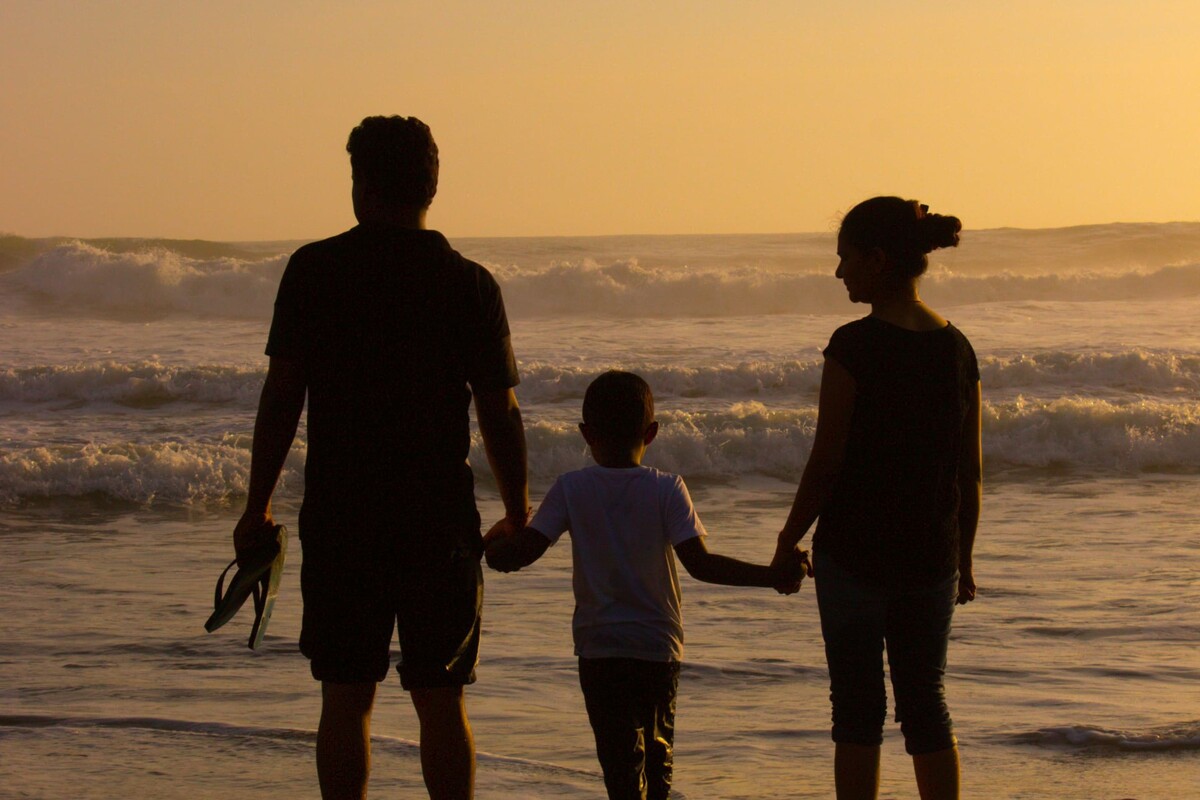 Silhouette einer dreiköpfigen Familie, die beim Sonnenuntergang am Strand steht.