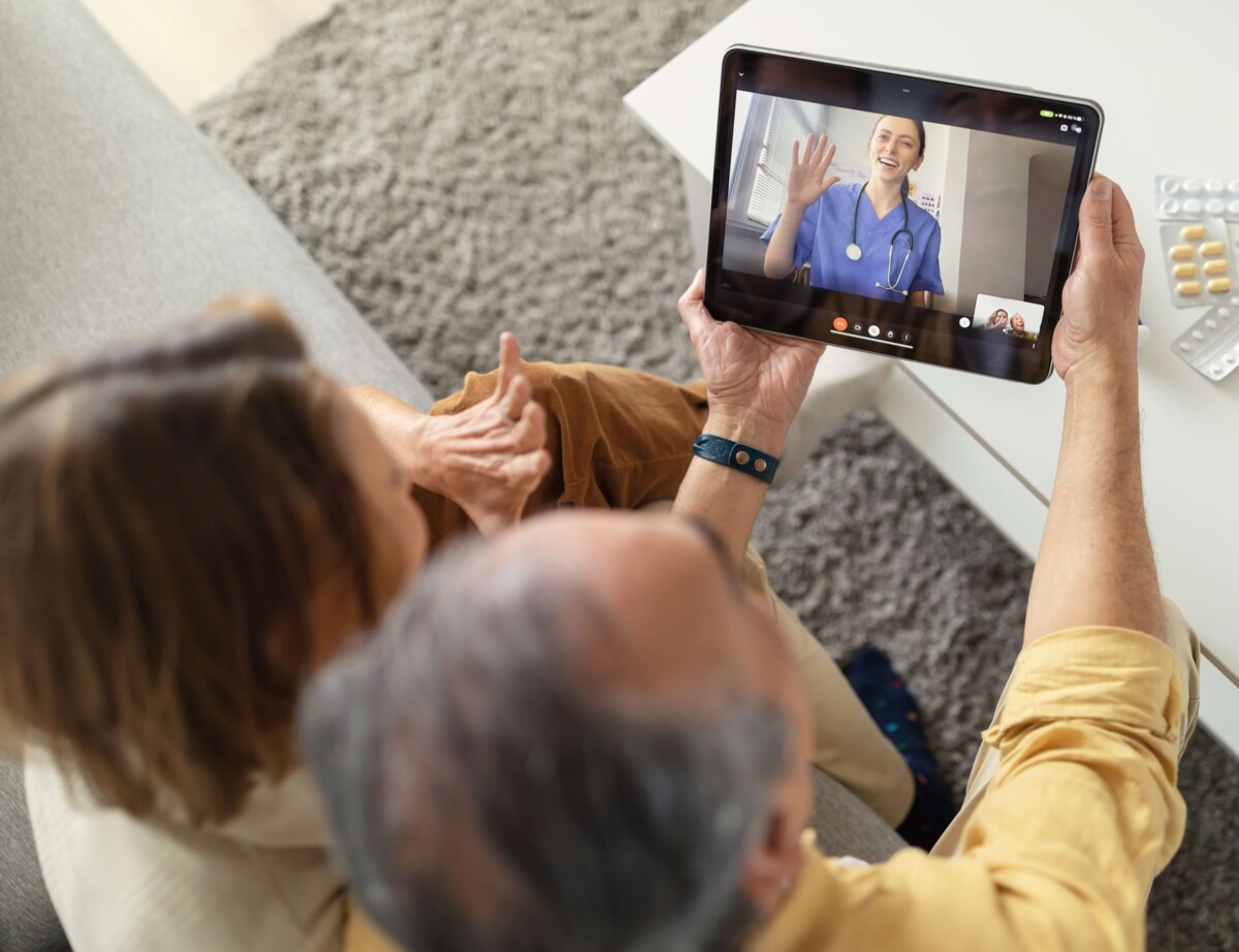 Ein älteres Ehepaar sitzt auf dem Sofa und führt einen Videocall mit einer Ärztin