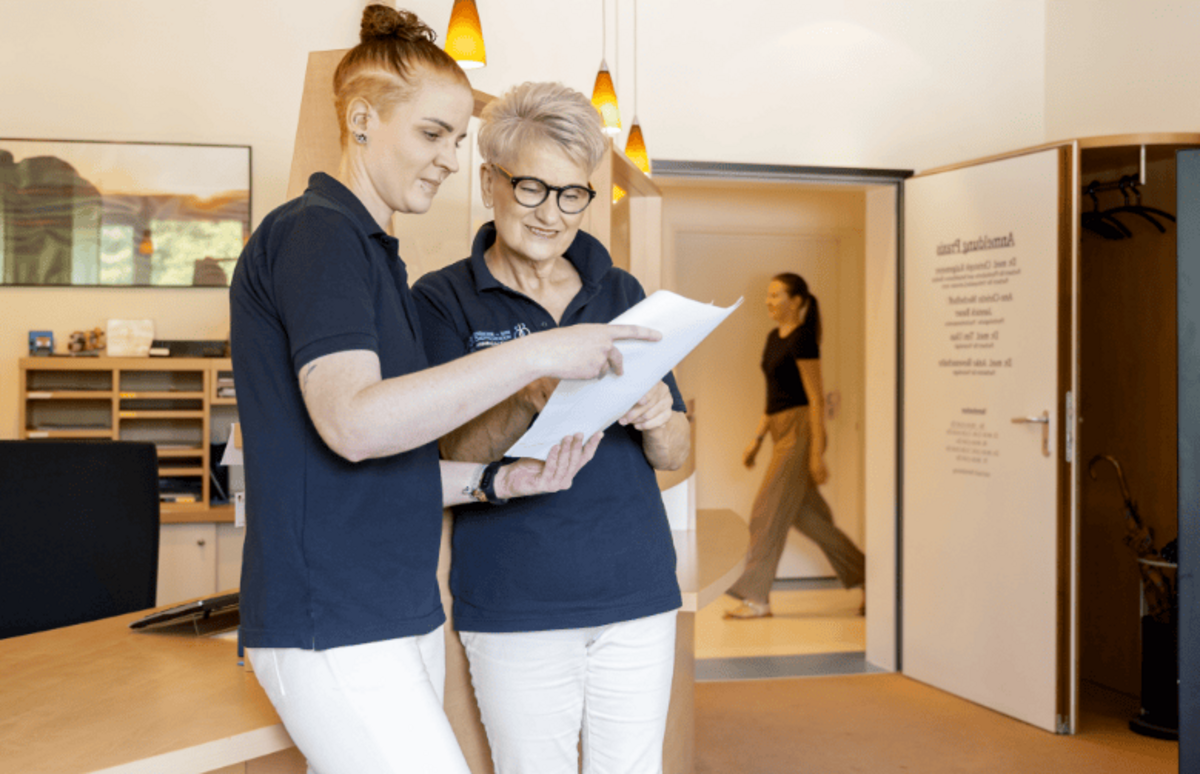 Zwei Mitarbeiterinnen stehen vor dem Empfang und schauen sie Unterlagen an